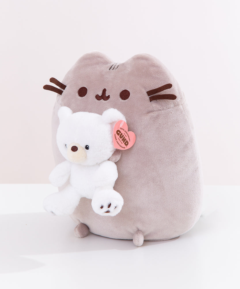 Quarter side view of the Pusheen x GUND plush. The sitting cat holds a small white bear with black eyes and embroidered paw pads.