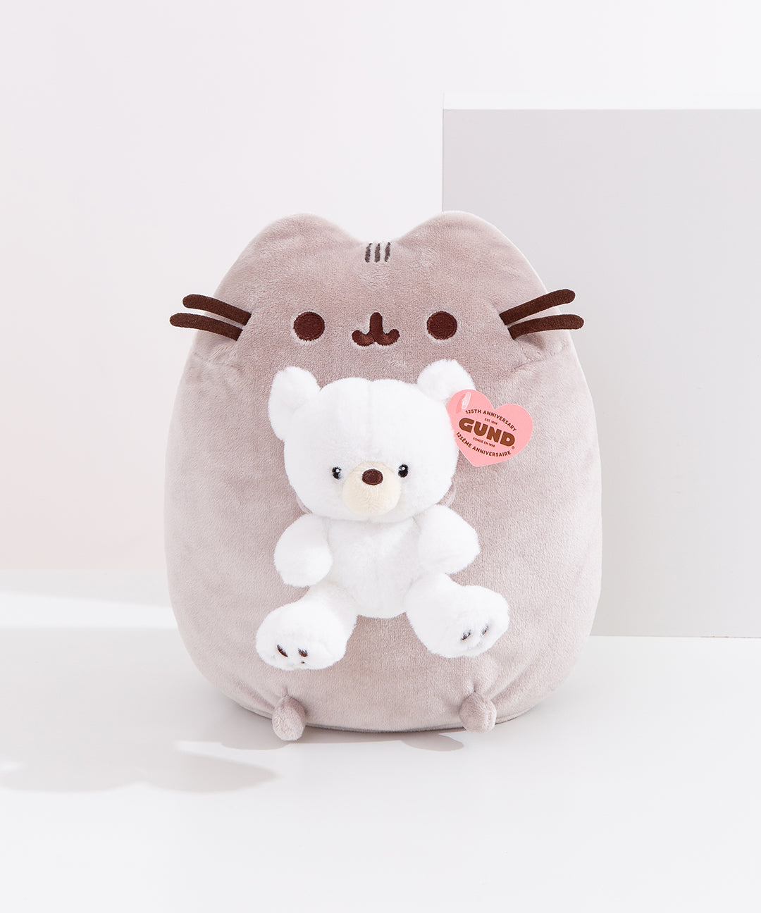 Front view of Pusheen x GUND Kai Bear Plush. The tabby cat sits upright holding a snow-white Kai bear, which is detailed with a cream-colored muzzle and embroidered paw pads.