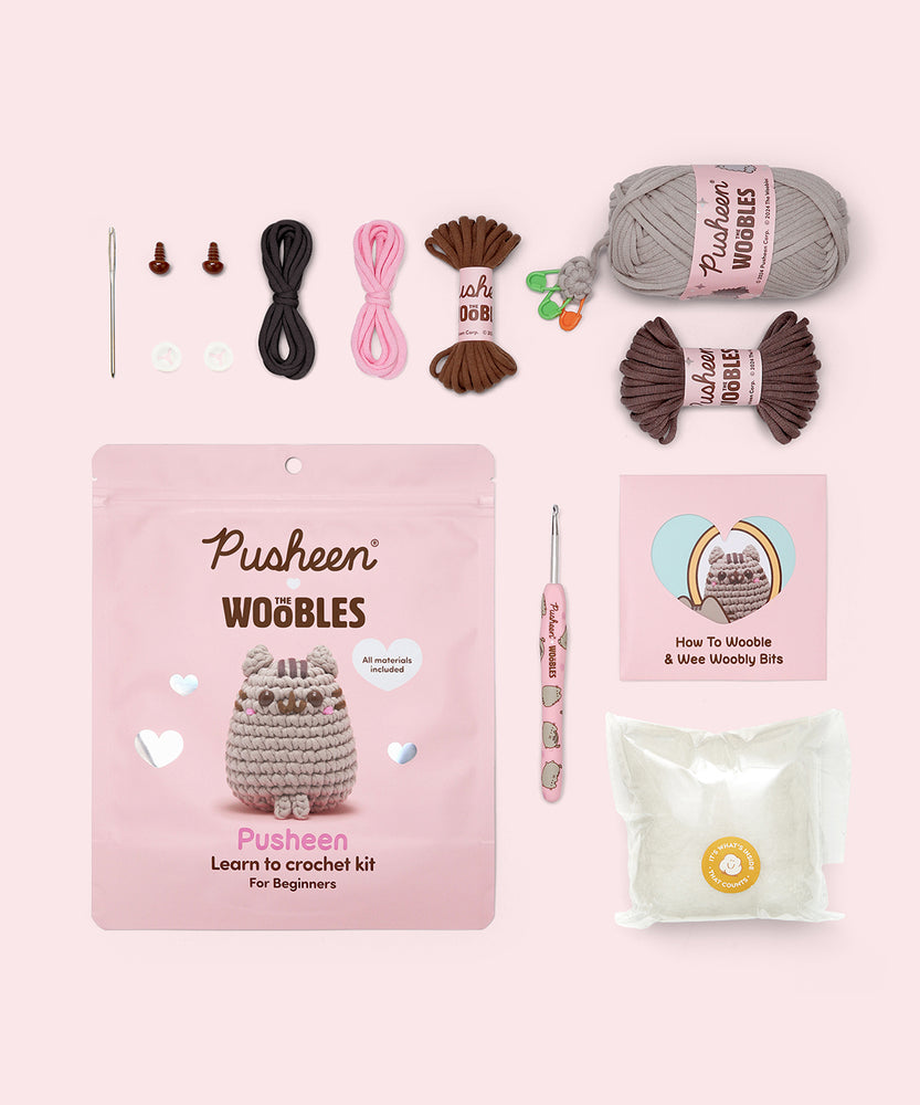 Contents included in the Beginner Pusheen Crochet Kit. The kit includes a needle, two plastic eyes, two clear buttons, all necessary yarn colors, a custom pink crochet hook, stuffing, and a how-to guide.