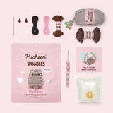 Contents included in the Beginner Pusheen Crochet Kit. The kit includes a needle, two plastic eyes, two clear buttons, all necessary yarn colors, a custom pink crochet hook, stuffing, and a how-to guide.