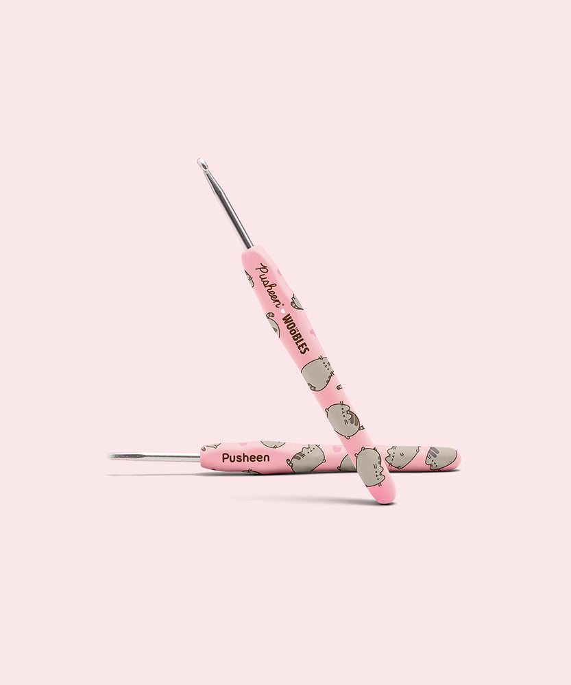 Close-up of the custom crochet hook. The pink handle features an all over print of Pusheen the Cat and the Pusheen x The Woobles collaboration logo. 