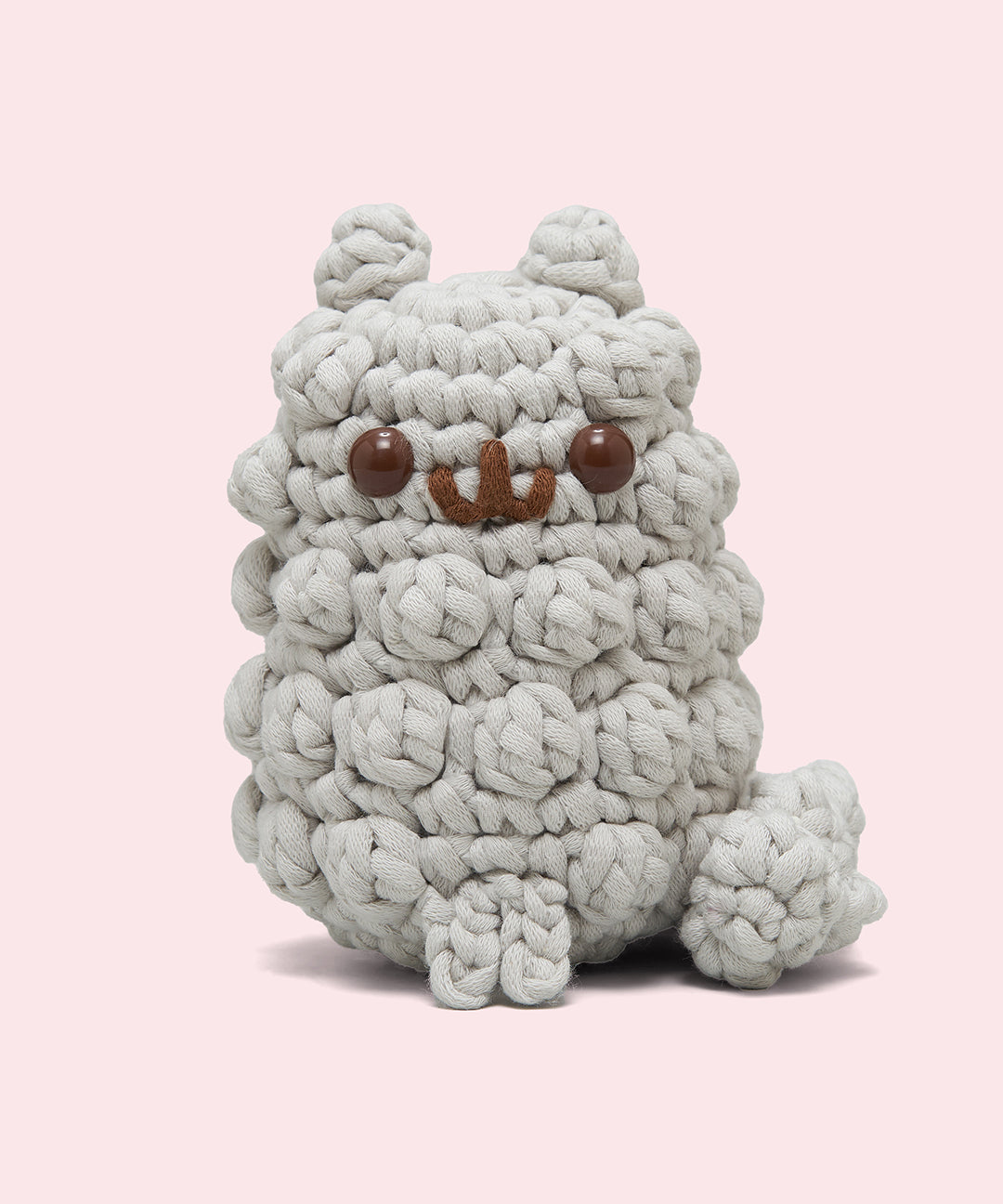 Front view of the Pusheen x The Woobles Stormy Crochet Kit. The light gray cat is crafted with yarn that mimics Stormy’s fluffy fur and tail. The plush stands on two legs and has a tail feature. 