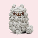 Front view of the Pusheen x The Woobles Stormy Crochet Kit. The light gray cat is crafted with yarn that mimics Stormy’s fluffy fur and tail. The plush stands on two legs and has a tail feature. 