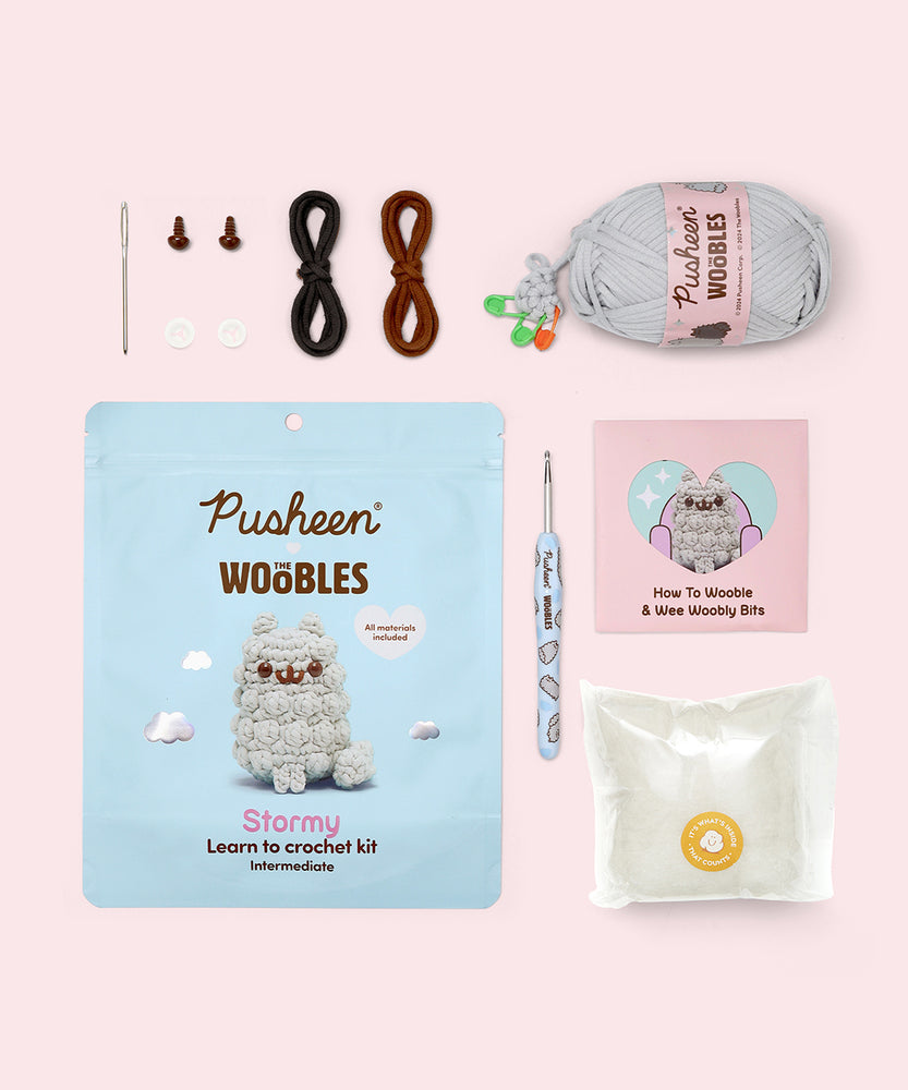 Contents included in the Intermediate Stormy Crochet Kit. The kit includes a needle, two plastic eyes, two clear buttons, all necessary yarn colors, a custom light blue crochet hook, stuffing, and a how-to guide. 