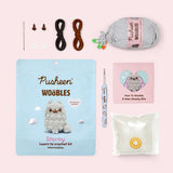 Contents included in the Intermediate Stormy Crochet Kit. The kit includes a needle, two plastic eyes, two clear buttons, all necessary yarn colors, a custom light blue crochet hook, stuffing, and a how-to guide. 