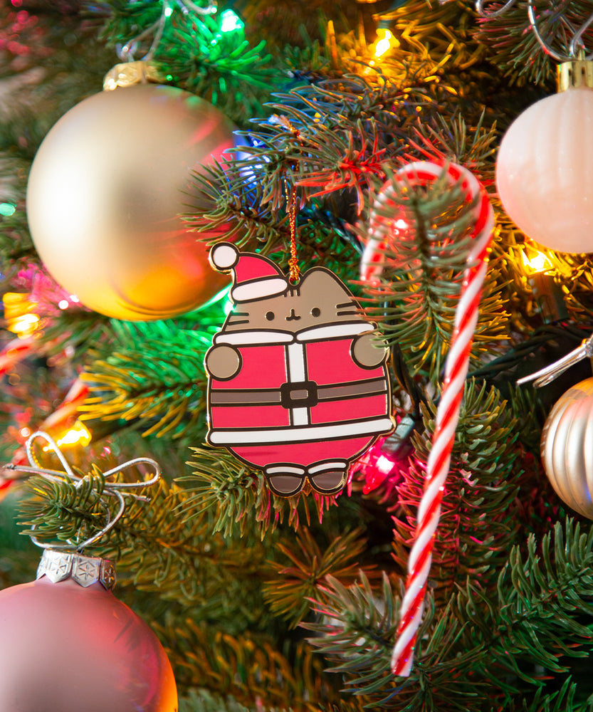 Santa Paws Pusheen Ornament hangs from a branch in a christmas tree decorated with lights, ball ornaments, and candy canes.