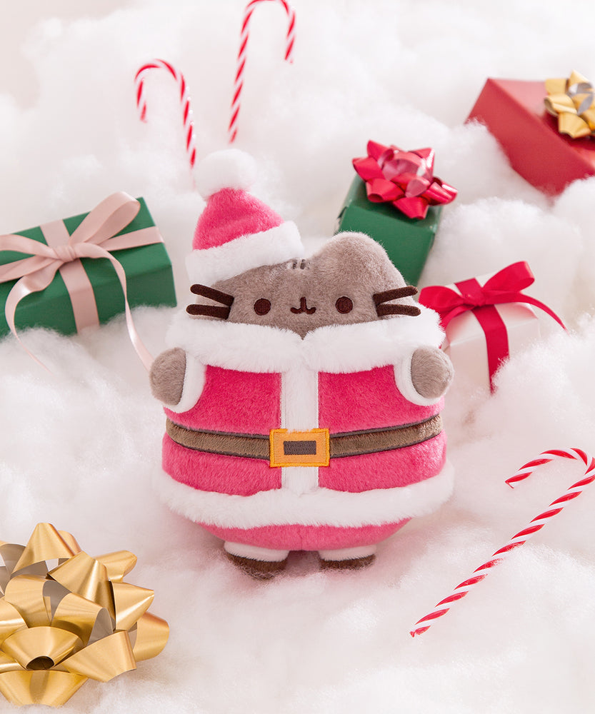 Plush toy cat in Santa outfit with Christmas presents and candy cane on a white fluffy background.