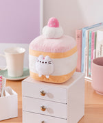 Cake Squisheen shown on a desktop to show scale of 7" tall plush toy. Pusheen the Cat rests inside the cream layer of the cake plush.