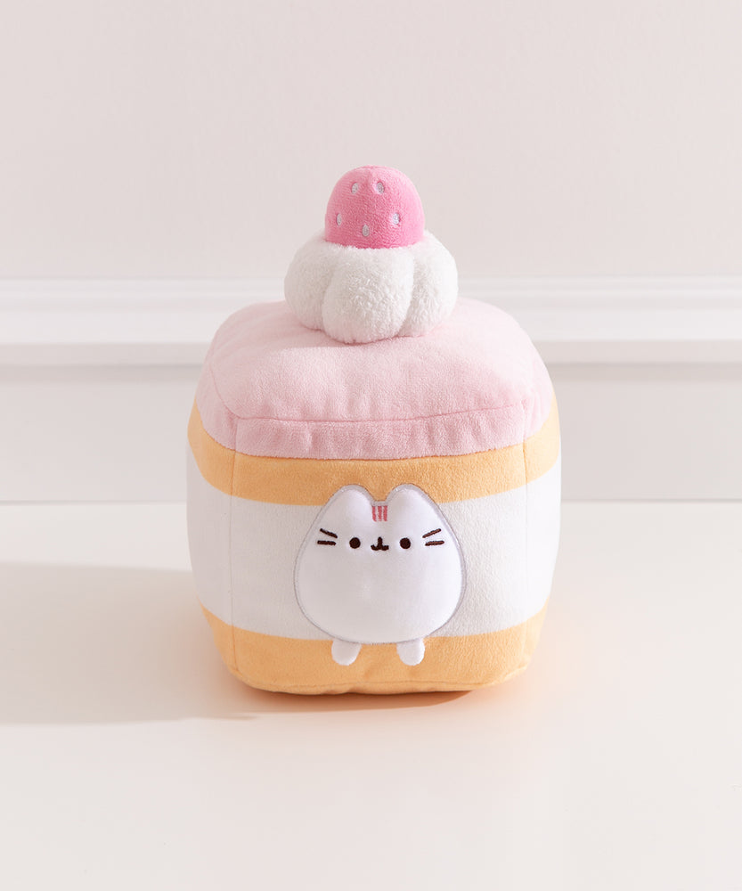 Pusheen Cake Plush is a layered strawberry sponge cake with alternating light yellow cake, white cream, and light pink icing. The cake is topped with a white textured whipped cream plush dollop and light pink strawberry with white embroidery to look like seeds.