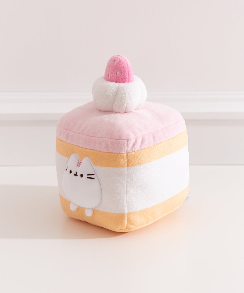 Side quarter view of the strawberry cake Pusheen plush. The cake plush has a light yellow cake layer in the top and at the bottom of the square plush. 