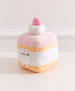 Side quarter view of the strawberry cake Pusheen plush. The cake plush has a light yellow cake layer in the top and at the bottom of the square plush. 