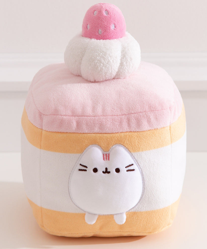 Cake Squisheen shown on a desktop to show scale of 7" tall plush toy. Pusheen the Cat rests inside the cream layer of the cake plush.