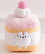 Cake Squisheen shown on a desktop to show scale of 7" tall plush toy. Pusheen the Cat rests inside the cream layer of the cake plush.