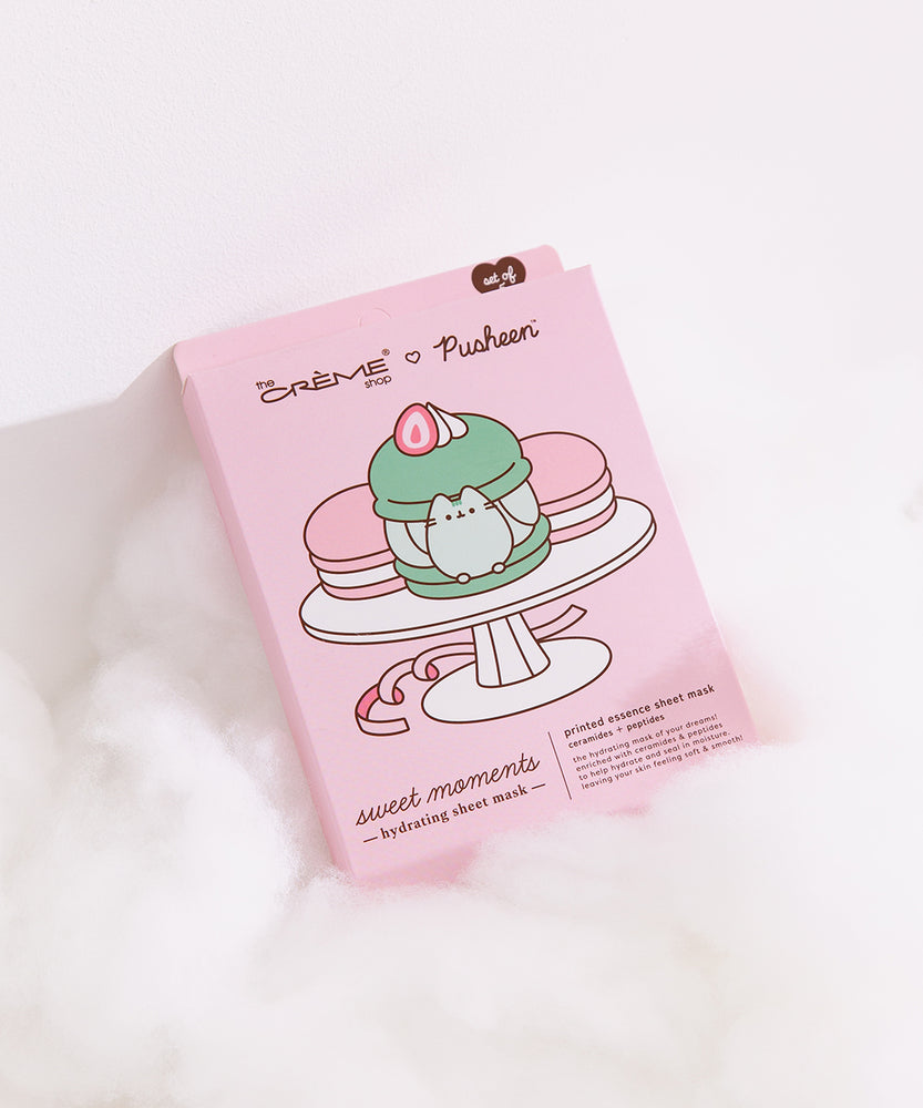 Pink sheet mask packaging box lies on white fluff. The packaging box shows graphics of three macarons on a dessert stand.