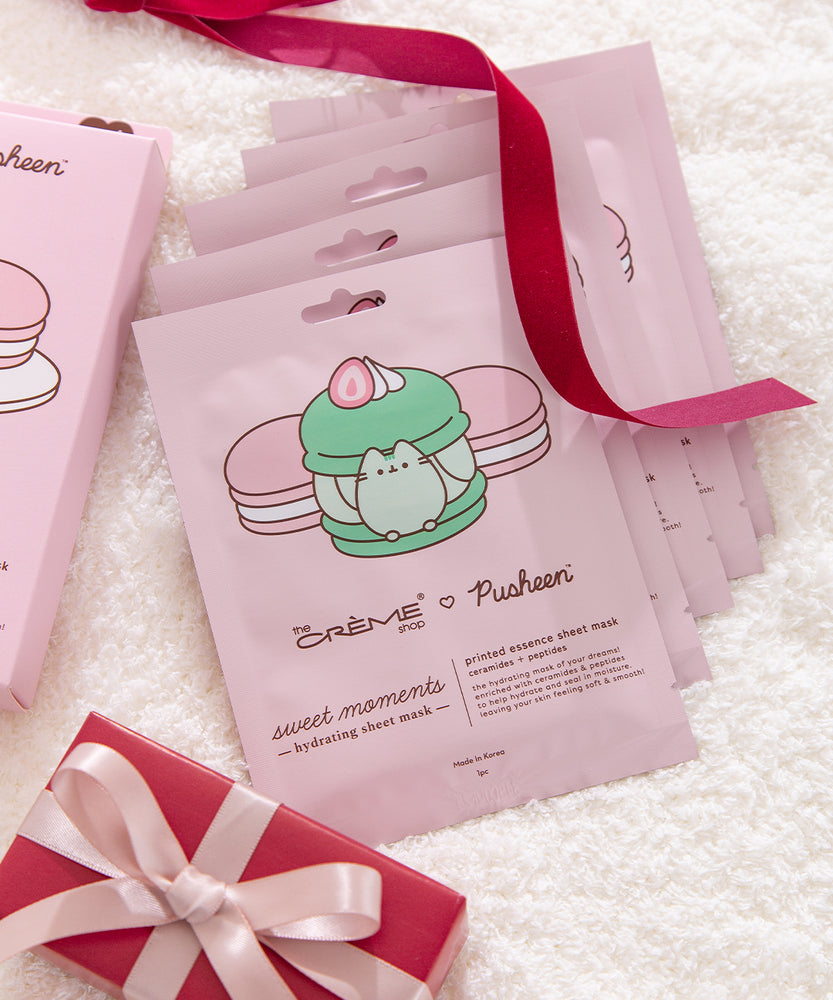 Pink sheet mask packaging box lies on white fluff. The packaging box shows graphics of three macarons on a dessert stand.