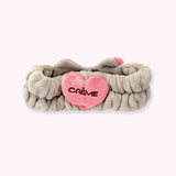 Back view of the plush headband. The stretchy grey grey headband features a pink plush heart with the Creme Shop logo.