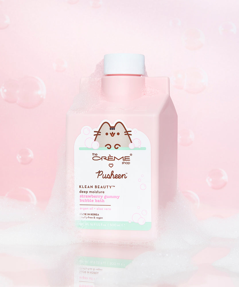 The Creme Shop x Pusheen Strawberry Gummy Bubble Bath in front of a light pink background with white suds. The pink pour top packaging mentions that the bubble bath contains argan oil and aloe vera and is apart of The Creme Shop's Klean Beauty collection.
