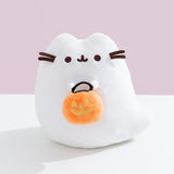 Front view of the white ghost plush that holds an orange candy pail that has yellow jack-o'-lantern details. The pail has two larger triangular eyes, a triangle nose, and a crooked carved mouth.