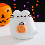 Front view of the Trick-or-Treat Boosheen Light Up Plush. The plush depicts Pusheen the Cat as a friendly ghost, Boosheen, and she holds a jack-o'-lantern candy pail.