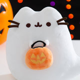 Close-up view of the Boosheen Halloween Light-Up Plush. The white ghost has Pusheen's classic eyes and mouth embroidered in dark brown. Pusheen the Cat's four 3D whiskers, two per side, extend off the plush sides. 