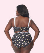 Model shows off the back of the swim top and bottoms. The print on the swimsuit includes pineapples, bananas, and strawberries.