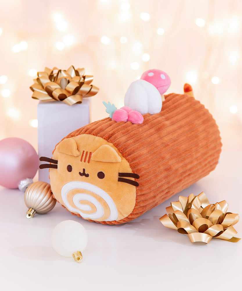 Side view of Pusheen Plush that is a Yule Log dessert. The brown cylindrical plush has festive Christmas toppings including holly berries, whipped cream, and a mushroom.  