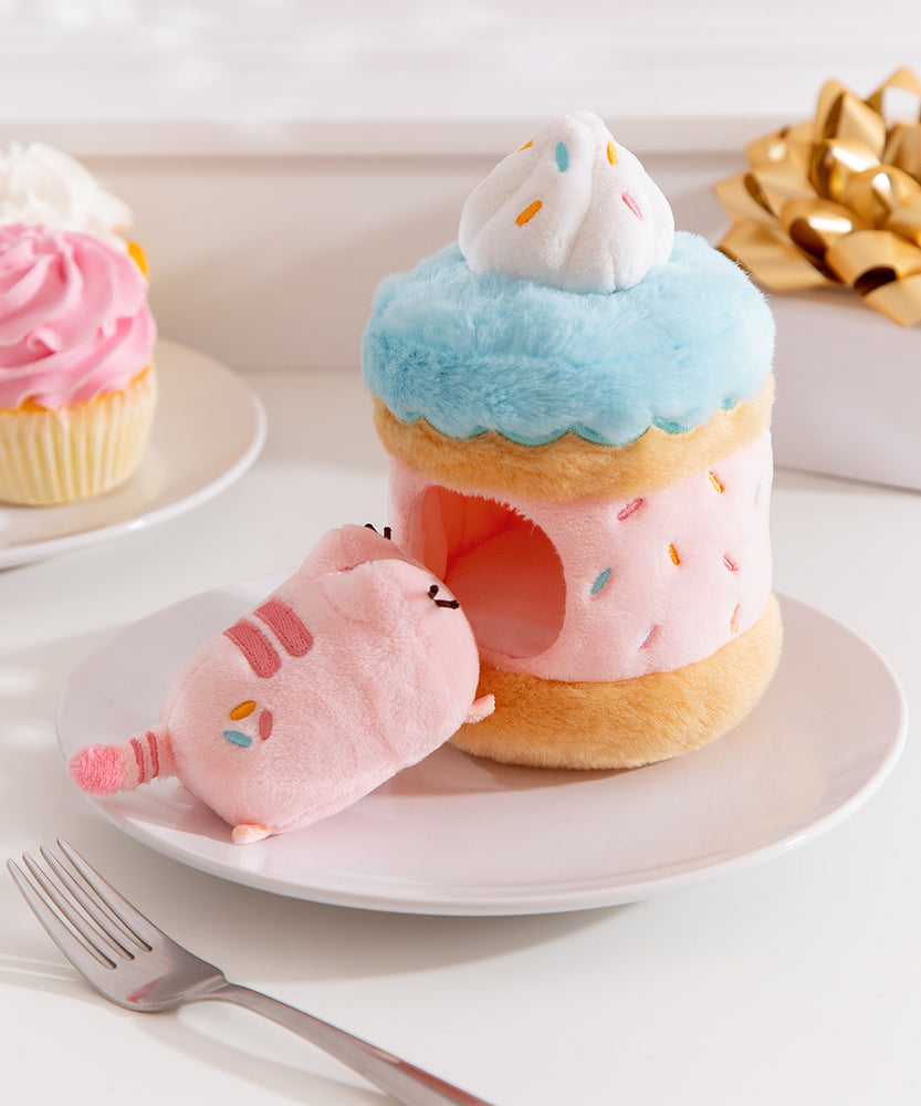 Side view of the Sprinkle Cake Plush. The removable interior plush rests in front of the cake environment. The little pink plush has multi-colored sprinkles embroidered on the booty area of the cat.  