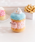 Side view of the Sprinkle Cake Plush. The removable interior plush rests in front of the cake environment. The little pink plush fits inside the front hole of the cake plush. 