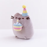 Quarter profile view of the Birthday Pushen Plush facing the left in front of a white background. Pusheen almost appears to be leaning forwards with her cake.