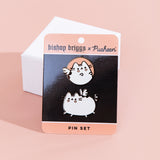 The Bishop Brigg x Pusheen Pin set in it’s original packaging leaning against a small square white pedestal, on top of a light orange background. The set includes two pins, one featuring a light orange circle with a white Pusheen with heart cheek marks and white wings inside, the other featuring a white Pusheen with black stripes galloping, pink heart marks underneath her eyes and two wings on top of her back that look like a butterfly.
