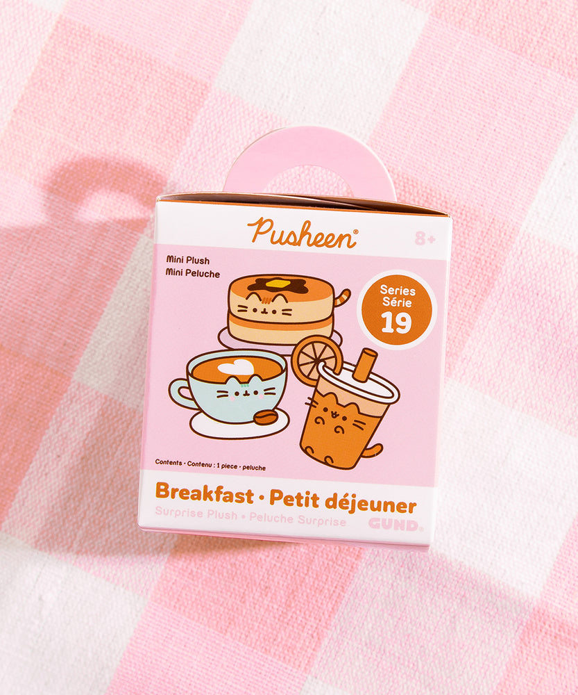 A close-up of the Pusheen Breakfast Surprise Plush packaging. The front of the packaging features Pusheen Breakfast characters: pancake stack, coffee latte, and orange juice. The packaging says that these Surprise Plush are mini plush. 