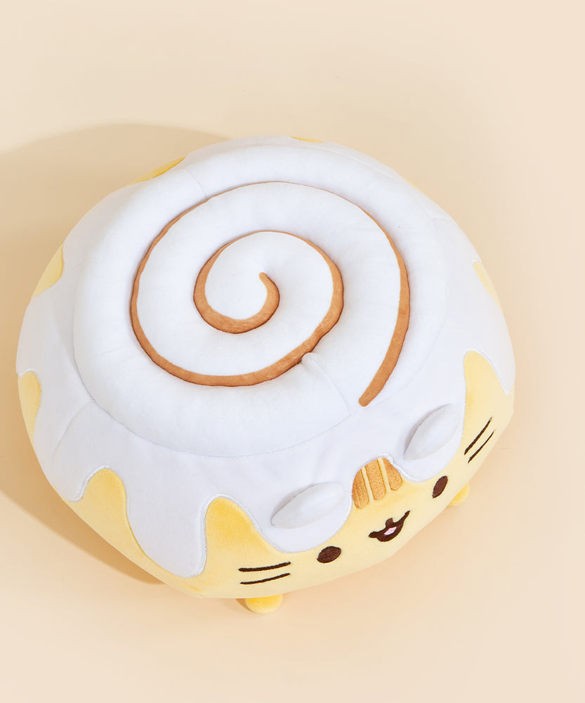 Top view of the Cinnamon Roll Squisheen in front of a cream background. The cinnamon swirl in the frosting is not embroidered, but leaves an indent in the frosting. The swirl starts at the same point as Pusheen's face, and swirls inwards.