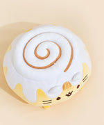 Top view of the Cinnamon Roll Squisheen in front of a cream background. The cinnamon swirl in the frosting is not embroidered, but leaves an indent in the frosting. The swirl starts at the same point as Pusheen's face, and swirls inwards.