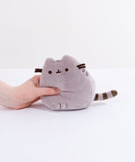 A model’s hand squeezing the grey Mini Squisheen Plush, demonstrating it’s squishiness.