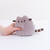 A model’s hand squeezing the grey Mini Squisheen Plush, demonstrating it’s squishiness.