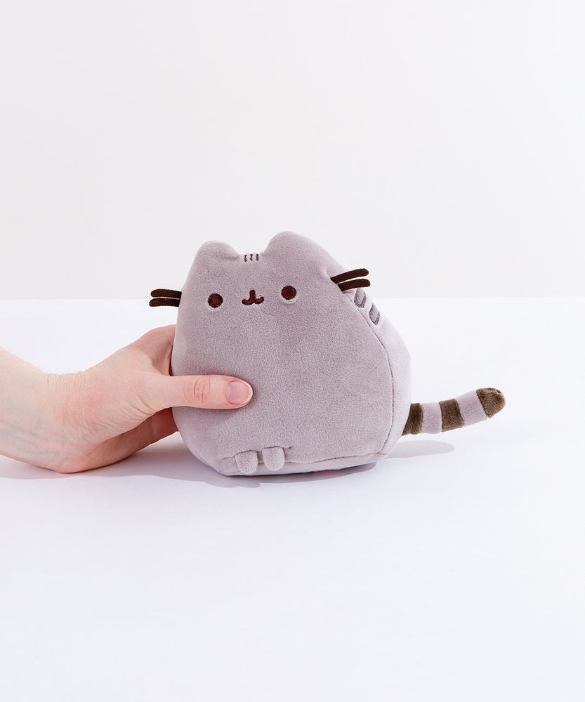 A model’s hand holding the Grey Mini Squisheen Plush in front of a white background. This plush is in Pusheen’s default colors.