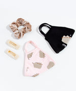 The Pusheen Hey Face Mask and the Pusheen Patterned face mask folded in half, laying besides each other and other accessories such as a scrunchie and two rectangular hair barrettes. 