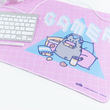 Angled close up of the Gamer Pusheen design on the Gaming Desk Mat. The white headphones, keyboard, and pen are partially visible, sitting on the left hand side of the mat. The Manufacturer details, copyright date and product number are visible on the lower right hand side of the mat.