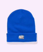 Front view of the Gaming Pusheen Knit Hat. The royal blue beanie lays on a light colored surface. On the folded edge of the beanie features an embroidered Pusheen the Cat with a pink gaming controller. 