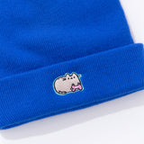 Close-up view of embroidery on the Gaming Pusheen Knit Hat. Pusheen is featured in her classic grey and light brown coloring. The cat holds a light pink gaming controller. The cat is outlined in a light teal thread.