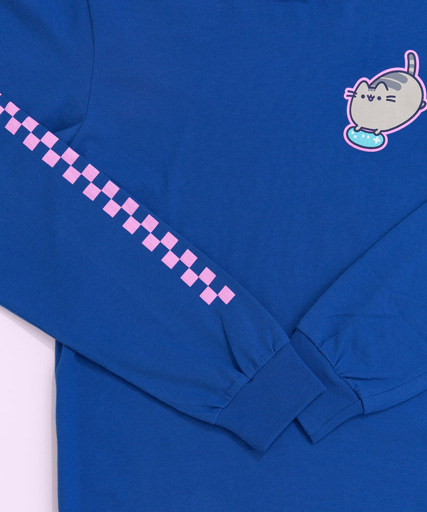 A close-up view of the tee’s screen print graphic. A pink grid is shown printed down on one of the sleeves of the bright blue tee. The graphic on the front of the shirt shows Pusheen the Cat surrounded by a pink outline while holding a light blue gaming controller. 
