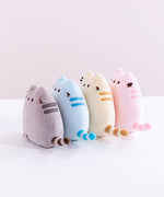All four Mini Squisheen Plush lined up against one another, facing the left. There are two darker stripes embroidered on Pusheen’s side, and her striped tail sticks out from the side. The color lineup starts with grey, blue, yellow, and ends with pink.