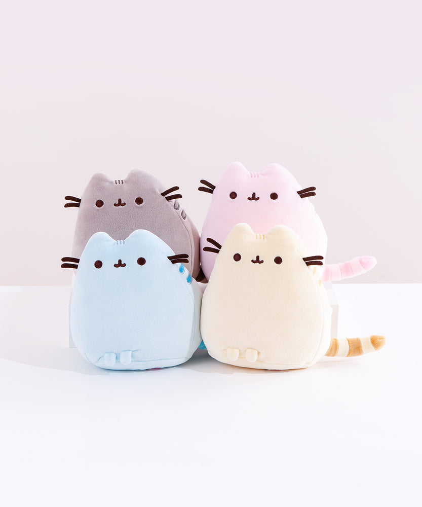 A quartet of Mini Squisheen Plush, all in the same pose with Pusheen in a more triangular shape, resting her feet at the bottom and her tail sticking out to the side. Each plush is a different color, including Pusheen’s classic grey, pink, blue and yellow.