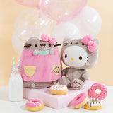The Pusheen and Hello Kitty collaboration plush sit together, A yellow background and pink and white balloons behind them, and donuts in front of them. A milk jug besides Pusheen features two striped straws.