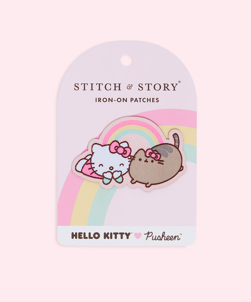 Front view of the Large Patch in it’s backing in front of a light pink background. The backing for the patch is light pink with a pink, yellow and mint rainbow passing behind the patch. The text ‘Stitch & Story Iron-On Patches’ is on the top near the backing’s display hole. At the bottom is a white rectangle with the Hello Kitty x Pusheen collaboration logo. 