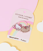 An embroidered patch featuring Hello Kitty and Pusheen wearing matching hair bows, laying on their stomachs together with a rainbow connecting the two friends. The patch is on a rounded carboard backing, laid on top of pink, yellow and white paper cutouts. 