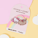 An embroidered patch featuring Hello Kitty and Pusheen wearing matching hair bows, laying on their stomachs together with a rainbow connecting the two friends. The patch is on a rounded carboard backing, laid on top of pink, yellow and white paper cutouts. 
