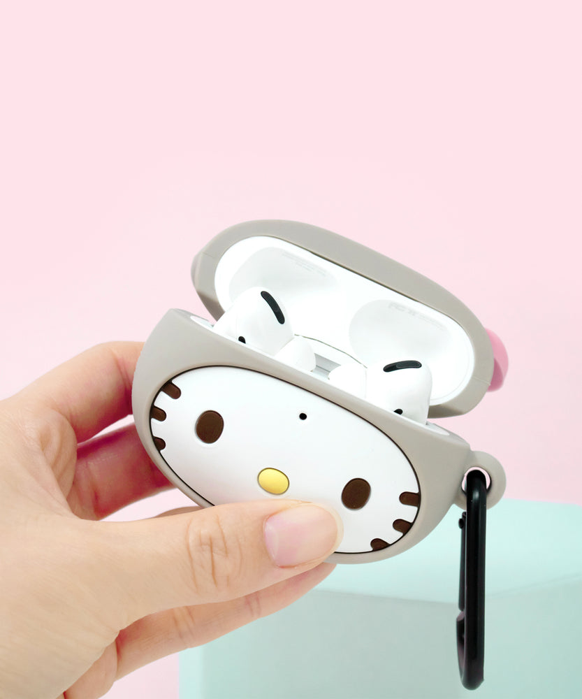 Hand holding an open Airpod case, showing the headphones inside. The case opens right above Hello Kitty's face. The interior of the case is white. There is a small black dot on the center of Hello Kitty's forehead. 