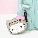 A small round silicone container the shape of Hello Kitty's head. Hello Kitty is wearing a grey hood with Pusheen's face on top, with Hello Kitty's signature pink bow by the right ear. On the right side is a round hoop where a black carabiner is attached. The Airpod case is hanging from a mint backpack, in front of a pink and white background.
