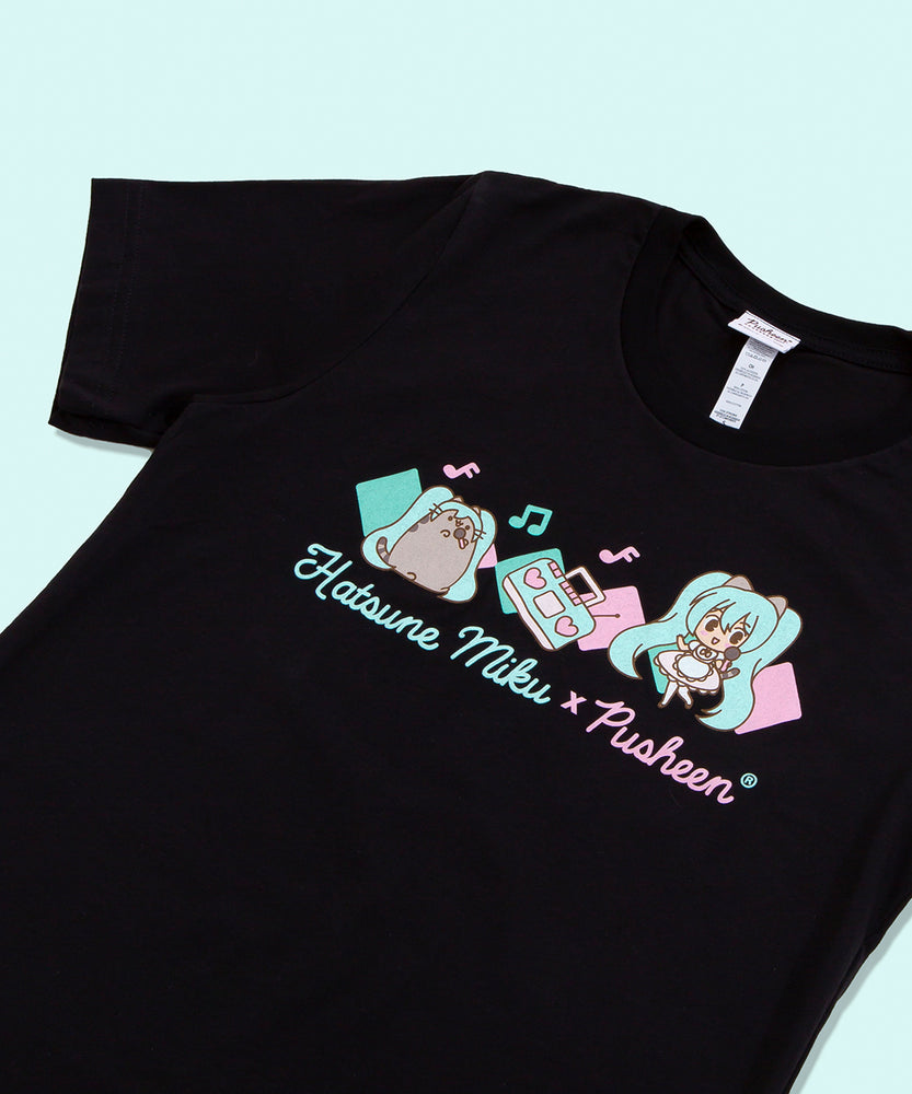 Close up of the graphic on the Boombox tee on top of a teal background. The boombox in the middle is leaning on it’s right bottom corner, and has hearts as speakers. The collaboration logo is all in cursive, with ‘Hatsune Miku’ in teal and ‘x Pusheen’ in pink. 